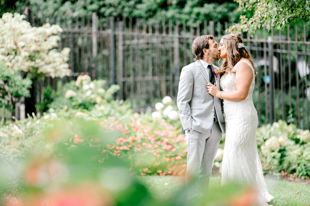 Groom and bride kiss outside with greenery and flowers. Posing tips for couples
