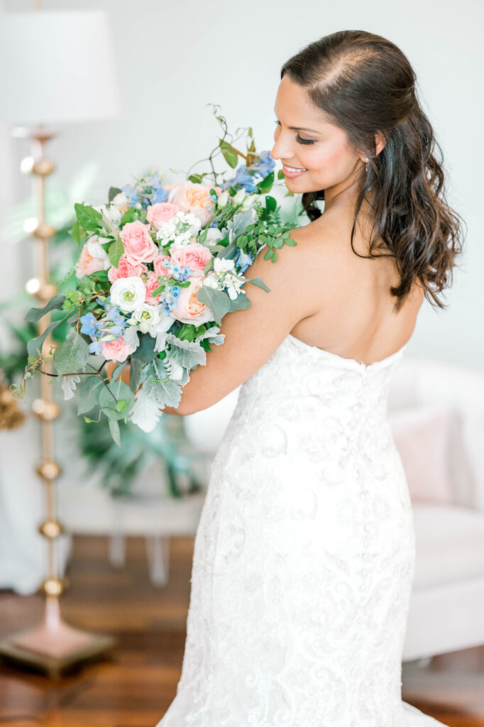 Wedding day essential - bridal bouquet. Bride smiles while holding her bouquet with white, pinkish orange, and blue flowers.